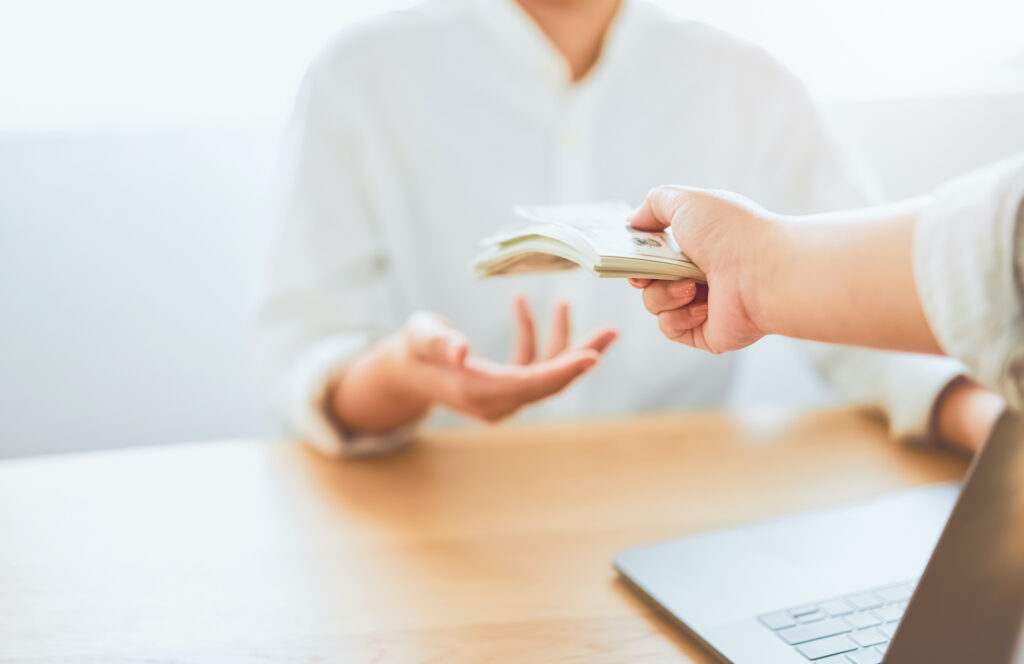 Close-up of hands giving dollar pay compensation from work. Give rewards as incentives for work, on office desk background.