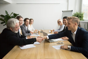 Young and old male partners shaking hands after signing contracts